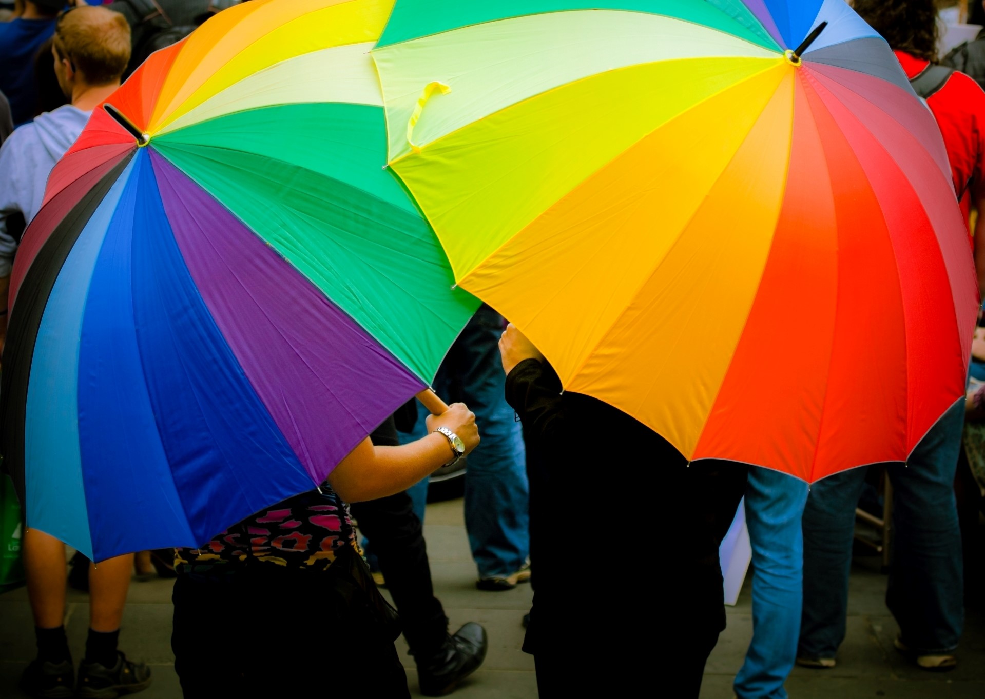 Two people holding rainbow umbrellas that cover them