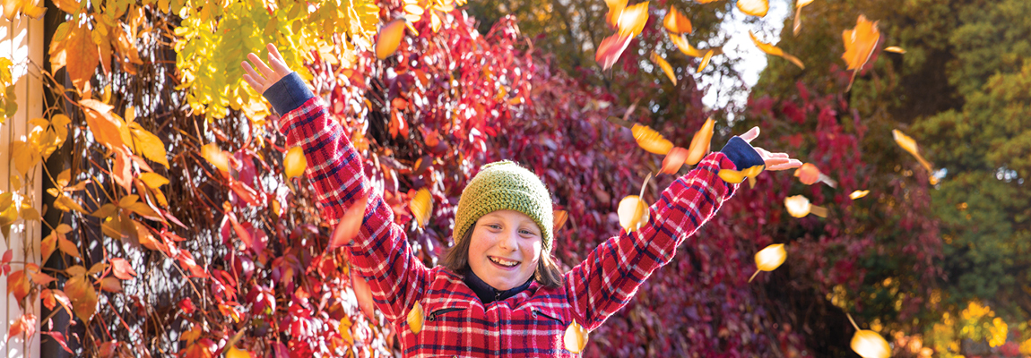 A person in a beanie holds up their hands in front of a wall of autumn leaves