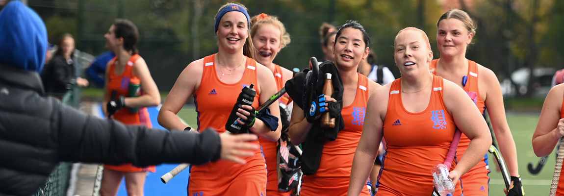 5 women in orange sportsgear approach a finish line