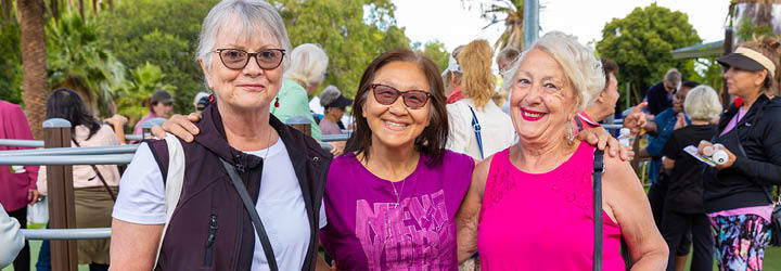 3 middle-aged women of different ethnicities smile with arms around each other