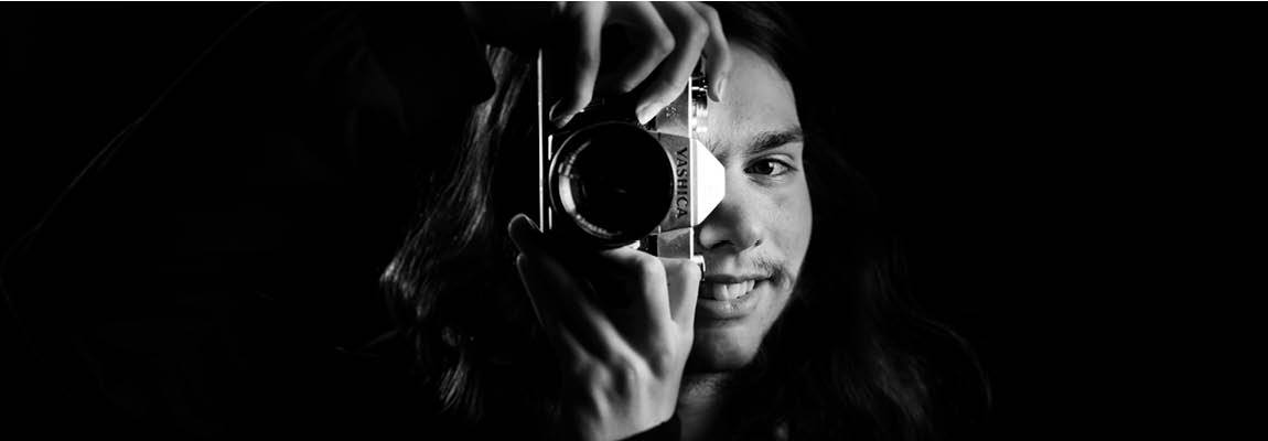 arty black and white photo of a man smiling as he holds a camera up