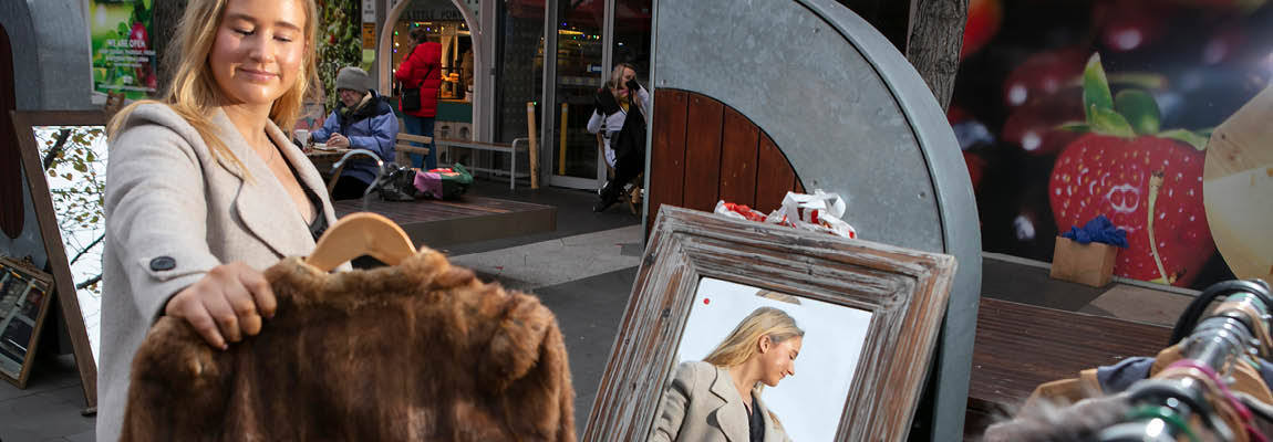 a person admires a coat and behind her is her reflection in a mirror
