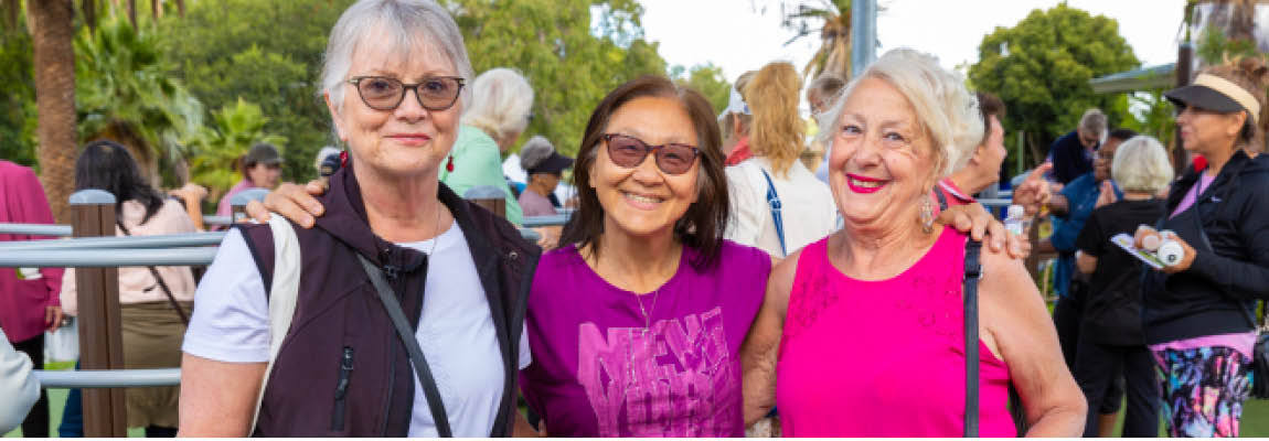 3 middle-aged women of different ethnicities smile with arms around each other