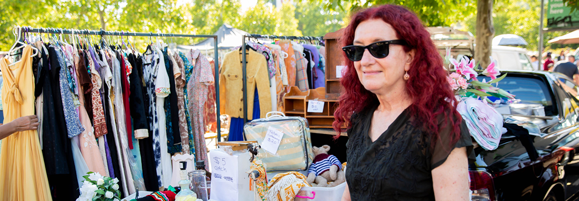 A person standing in an outdoor marketplace in front of secondhand clothes and items for sale