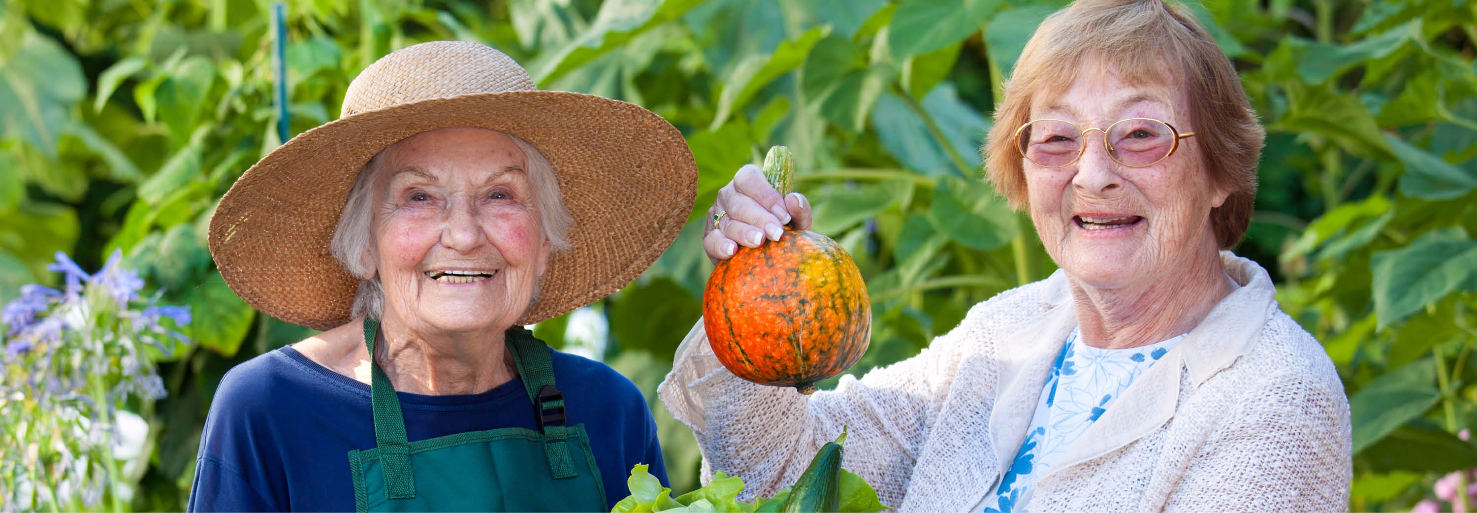 2 older women hold up a tiny pumpkin in a garden