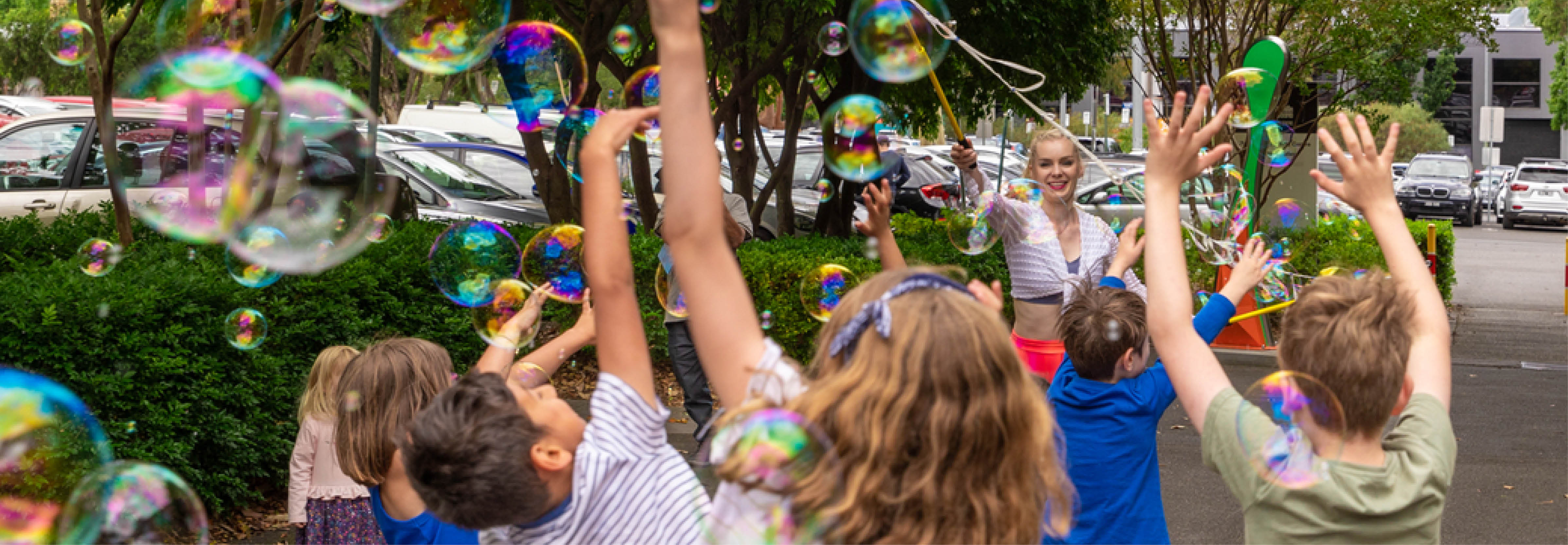 Children reach up for bubbles being blown by a young woman