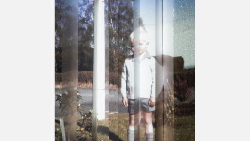 a streaky image of a child standing on the grass, a suburban street behind them