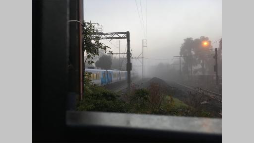 Photo by Liam Morris looking out on train tracks on a misty morning with a train moving past empty tracks