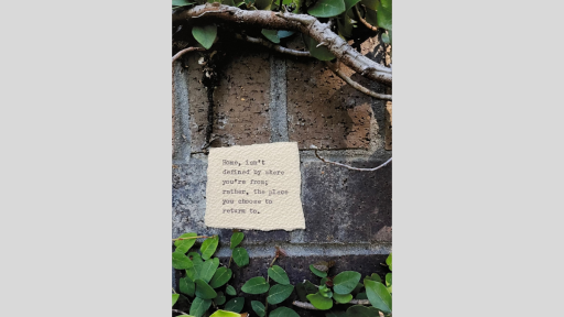A piece of torn paper with a poem printed from a typewriter, stuck to a brick wall outside with vines and green leaves below and above the paper