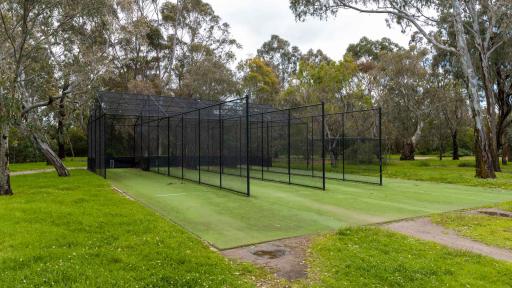 Cricket nets with 4 lanes divided by tall black fences. There are tall trees across the background.