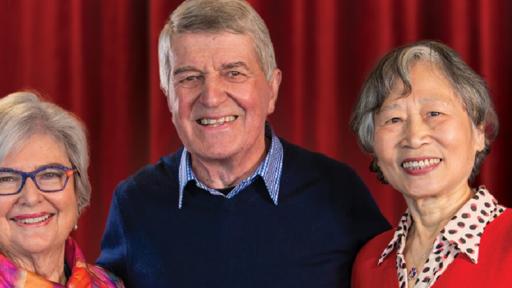 3 older people smile in front of a red velvet curtain
