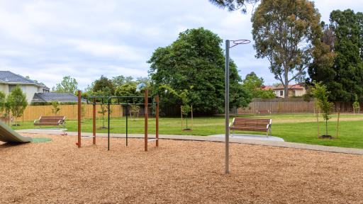 playground showing climbing frame with seat in the background and a grassy play area with trees