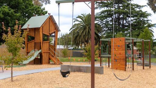 Playground showing two swings in foreground and timber combination unit with slide in background