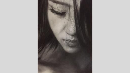 Graphite pencil artwork of a woman’s face. She is looking down, and her long black hair covers the right side of her face. She is wearing black eyeliner and mascara and her mouth is closed. 