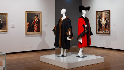 mayoral robes including a hat. Paintings on the walls behind of previous municipal mayors wearing the robes