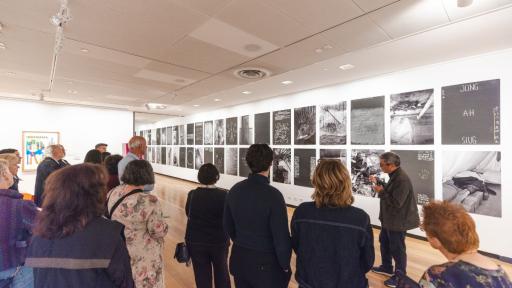 A group of people facing a long wall of large black and white images. Images include landscapes, portraits, text and abstract shapes