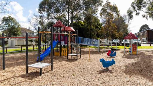 A playground featuring a slide on a mulch ground. Trees and grass are in the background.