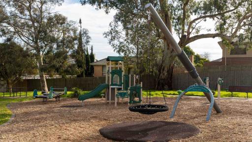 A kids playground featuring a slide and a swinging basket. The ground is mulch.