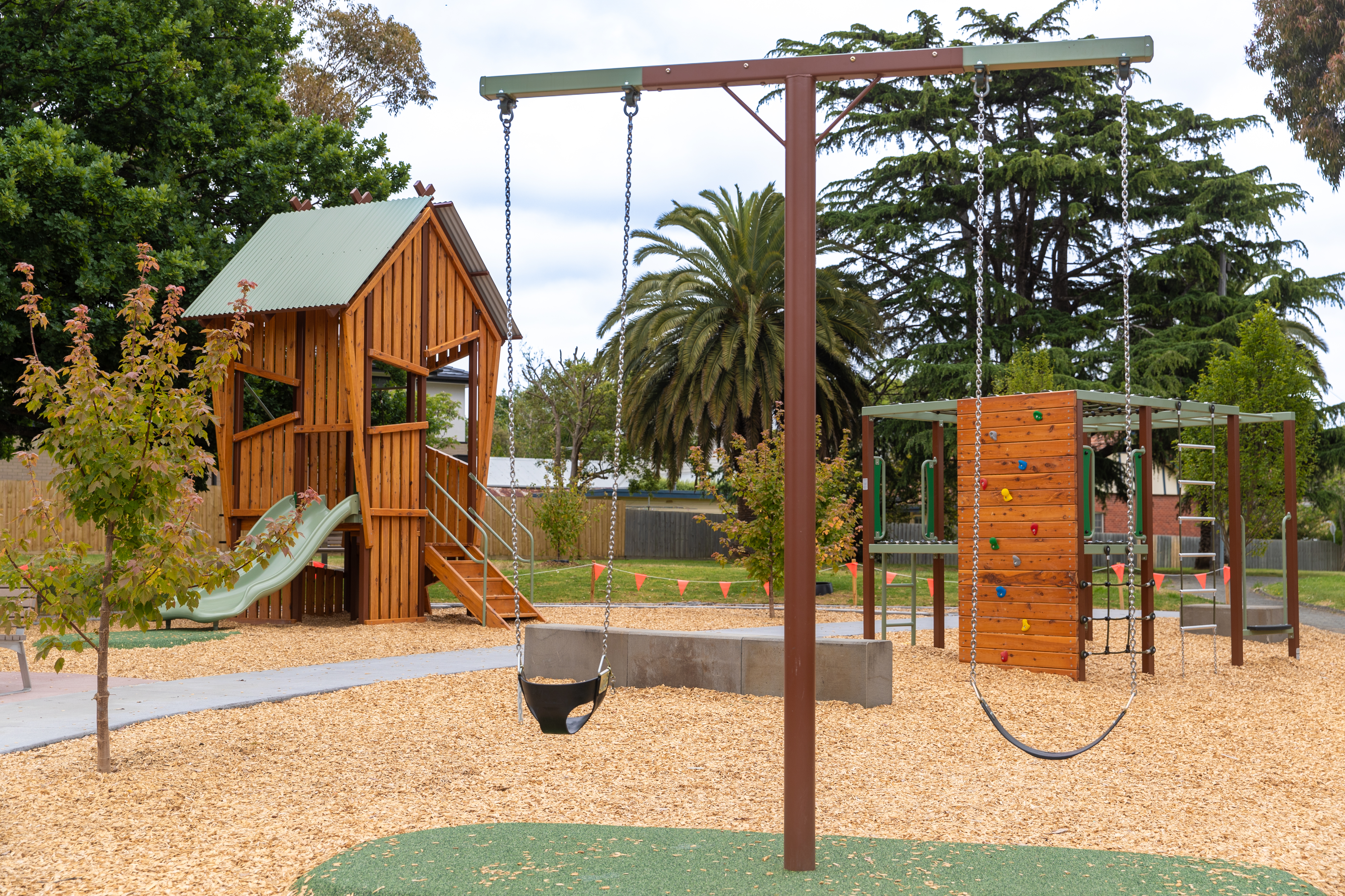 Playground showing two swings in foreground and timber combination unit with slide in background