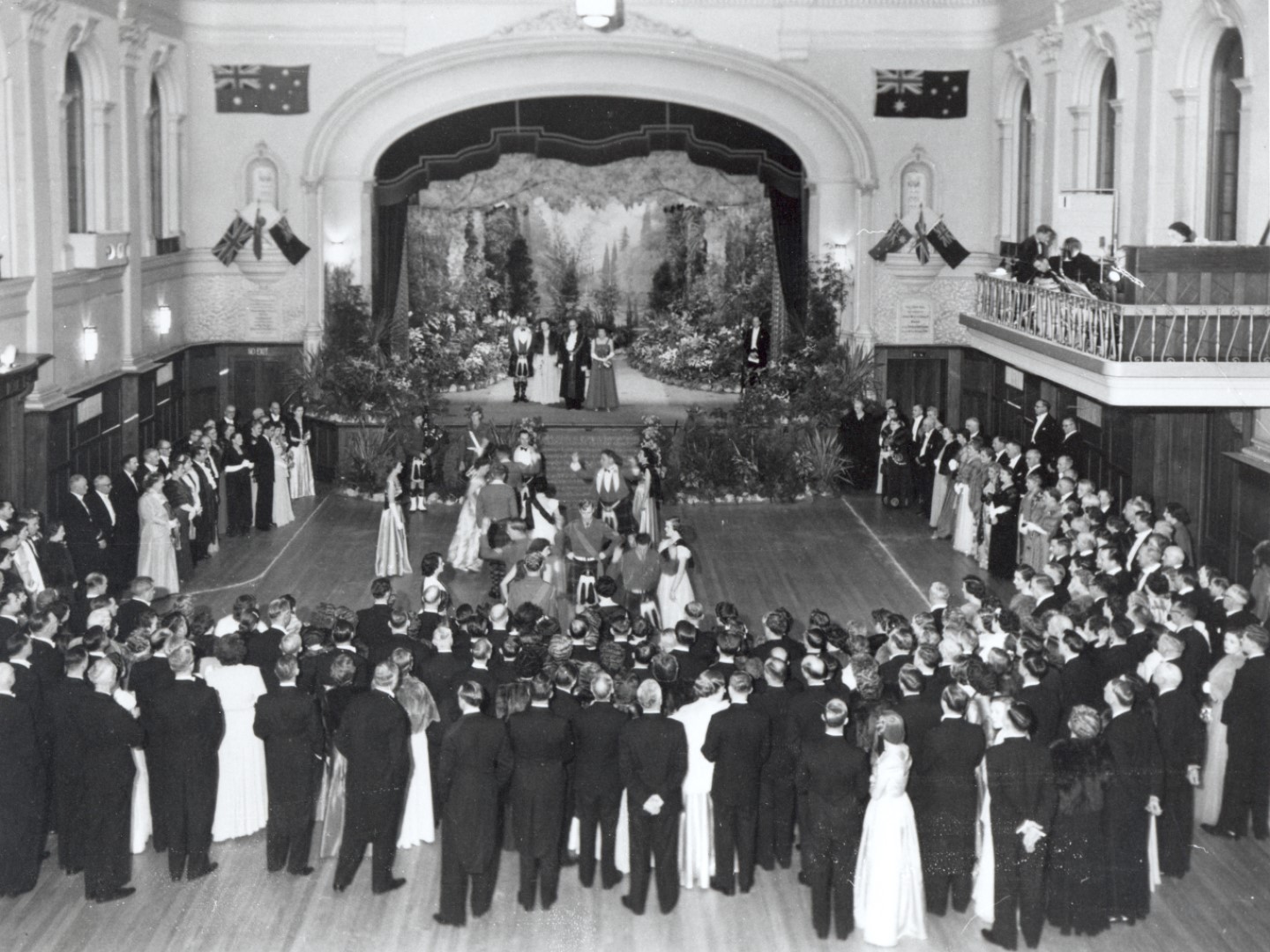 elegantly dressed men and women standing around the edges of the Main Hall at Hawthorn town hall. In the middle of the space are dancing couples