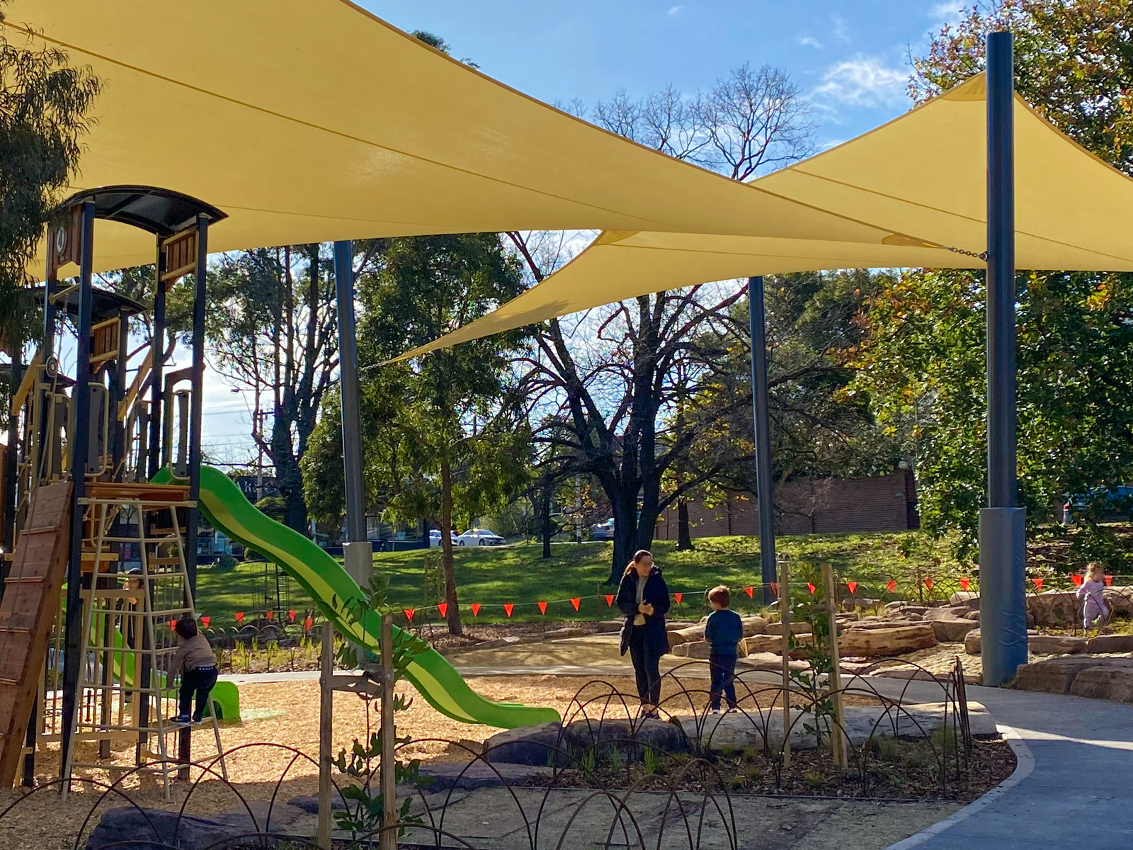 A woman and child stand beneath shade sails in a playground 