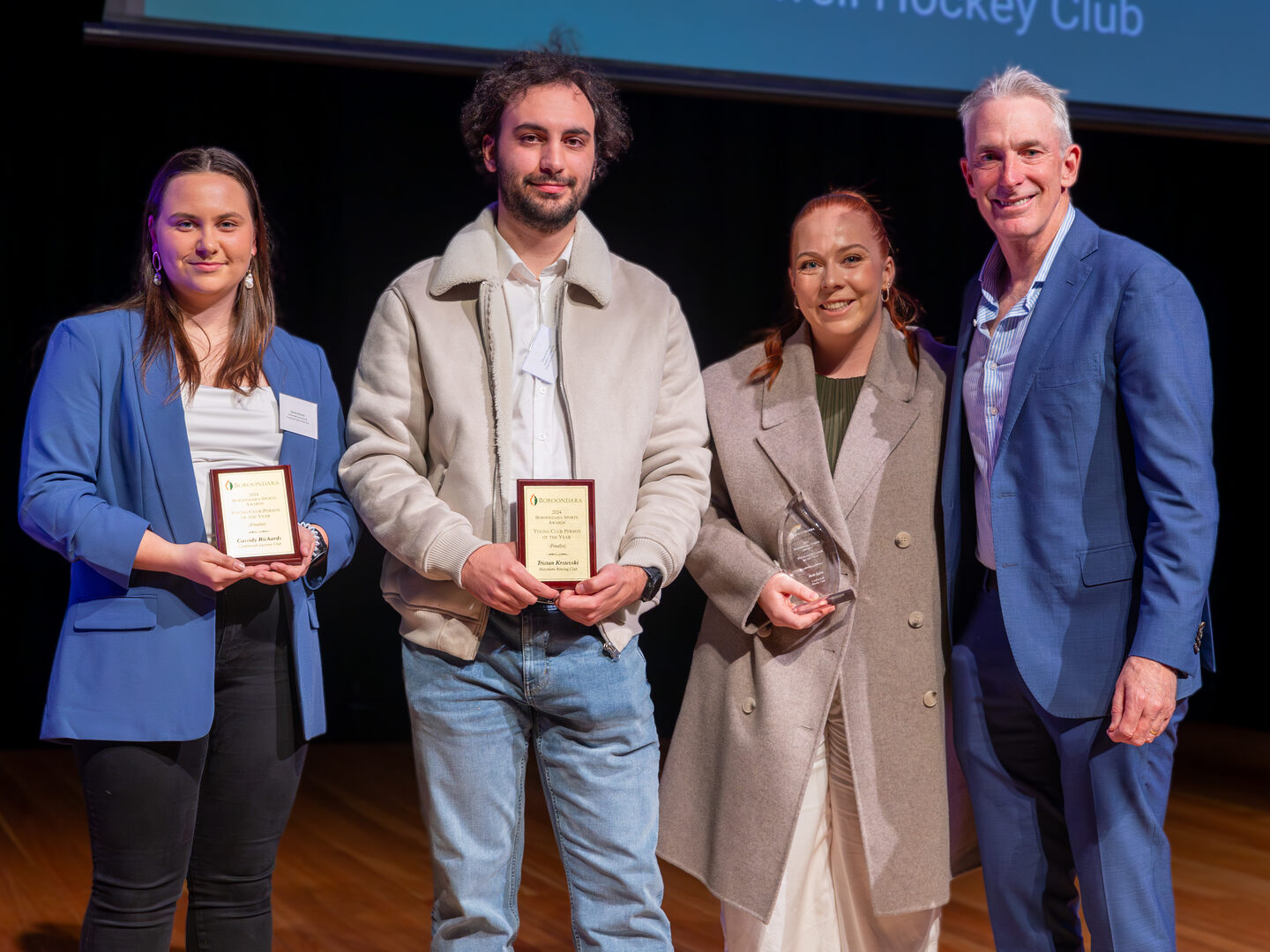 Four people standing smiling at the camera. Two of the people are holding plaques. 