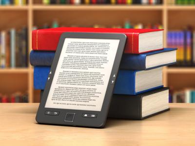an ebook reader leans against a pile of hardcover books