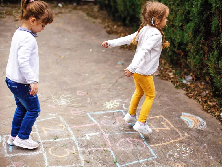 2 girls play hopscotch