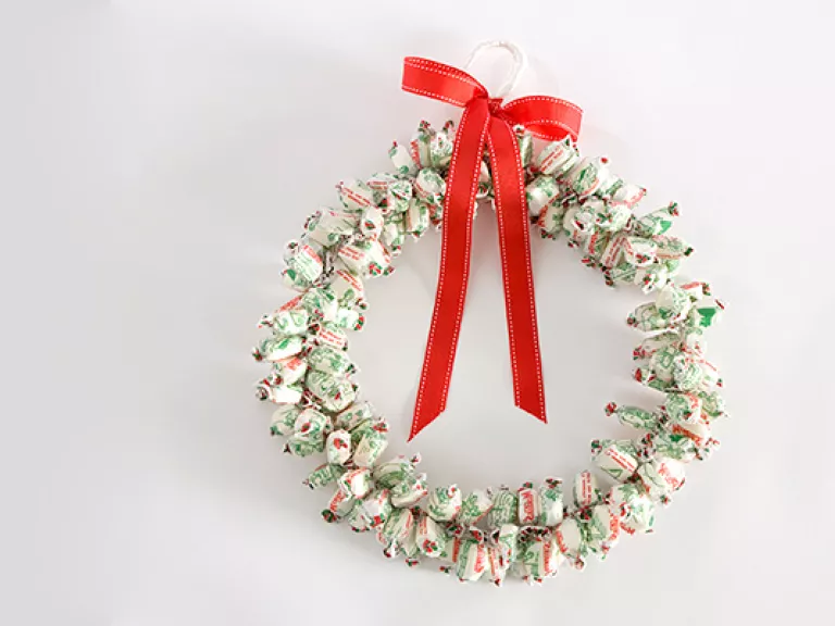 Christmas wreath made out of lollies with a red bow on a grey background.