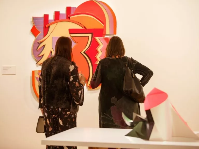 Visitors to 'Light Gestures' looking at a mixed media artwork made up of abstract geometric shapes.