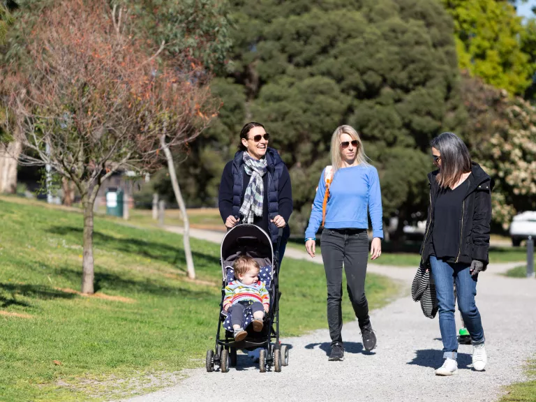 Three women walking on a footpath with one of them pushing a pram