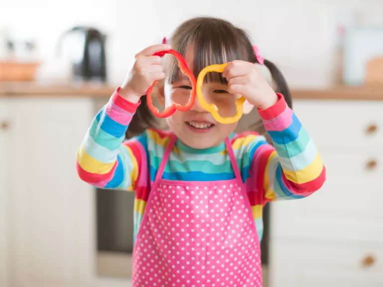 A toddler holds two cut pieces of capsicum up over her eyes