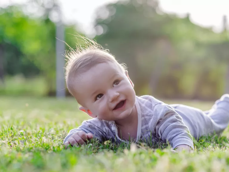 Smiling baby lying in grass looking up 