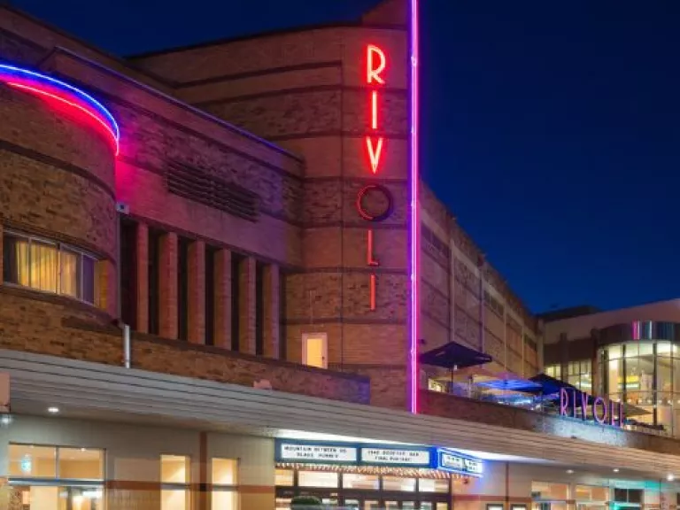 The Rivoli theatre at night showing the red and blue neon lights, the lit entrance, and cars moving past