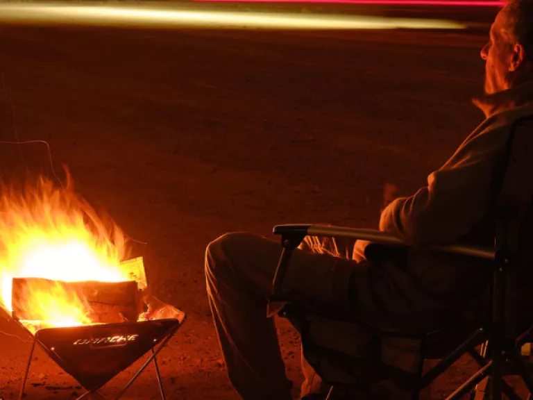 A man sits in a camp chair beside a campfire in a small drum