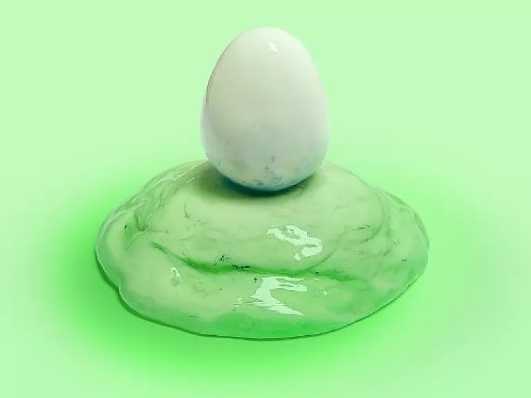 Ceramic sculpture of a white egg on a light green mound.