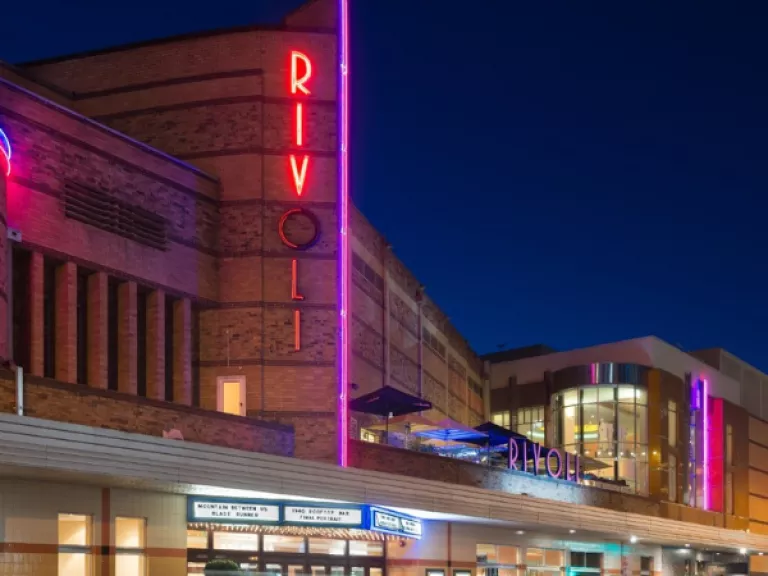 Front of Rivoli Cinema building at night, with first 3 letters of Rivoli lighting up.