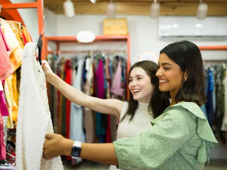 2 young women happily rummage through clothing racks