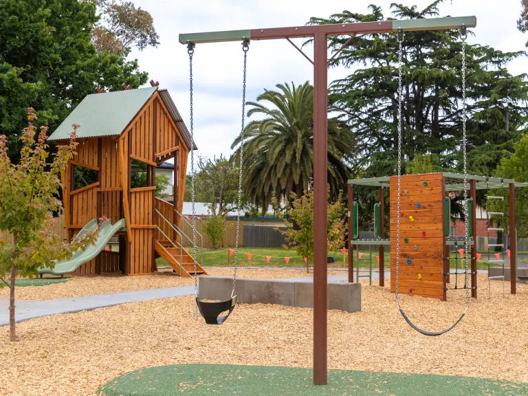 Playground showing two swings in foreground and timber combination unit with slide in background