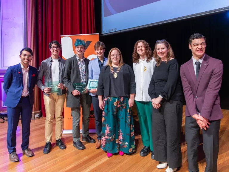 A group of 8 people standing together at an awards ceremony, some holding glass trophies.