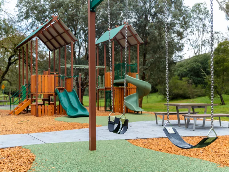 2 swings at a playground with climbing frames in the background