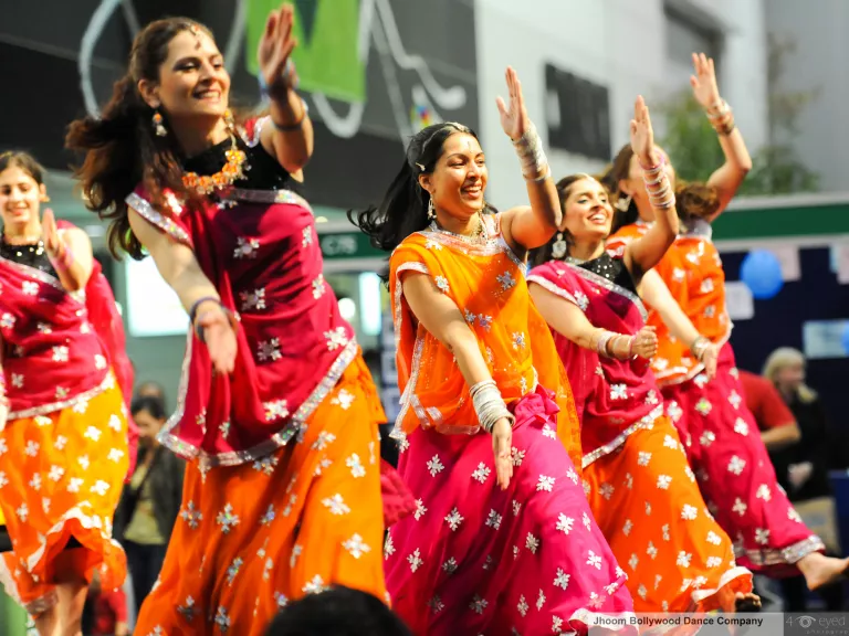 a group of bollywood dancers wearing yellow and pink smiling as they dance