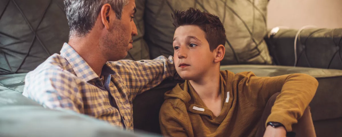 Man and young child sitting against a couch talking to each other