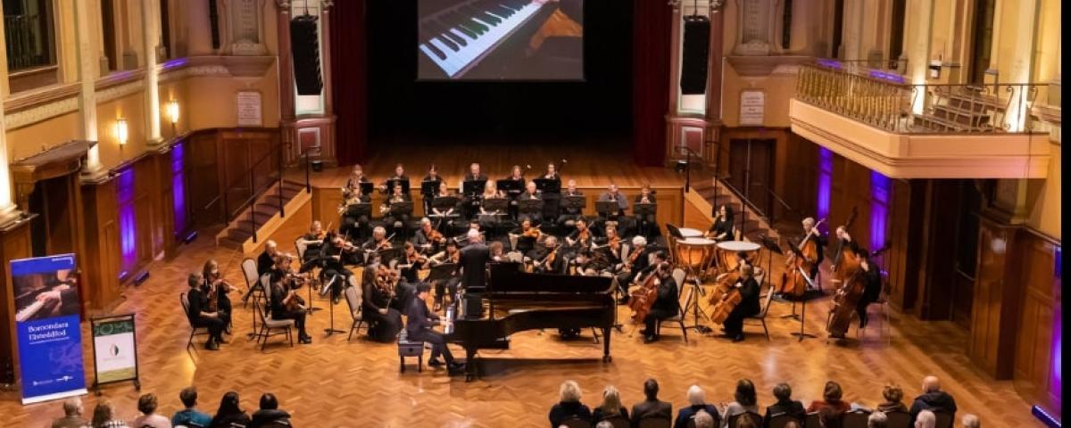 A piano concerto performance with a large band at the front of a formal hall