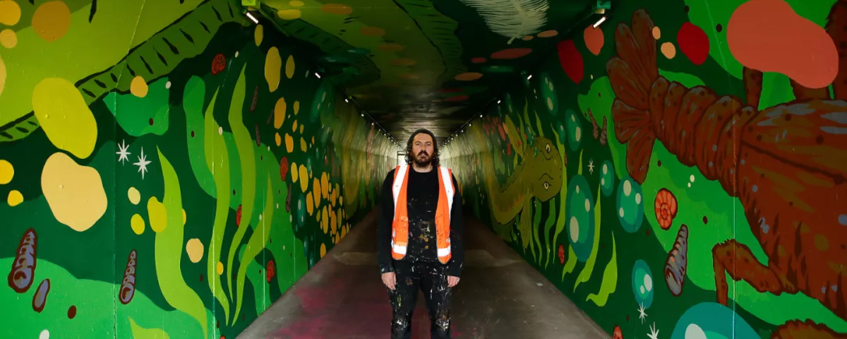 Person standing in the middle of an underpass painted with river creatures