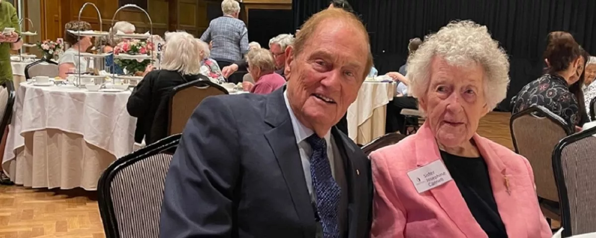 Two well-dressed senior citizens seated in a room with banquet tables