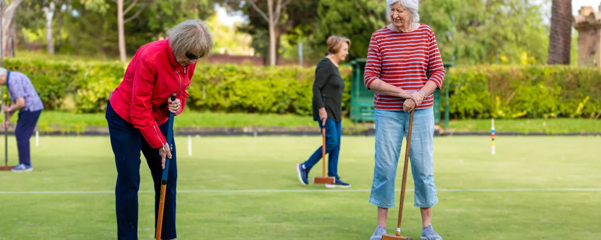 Several players on croquet green with one about to hit blue ball with mallet.