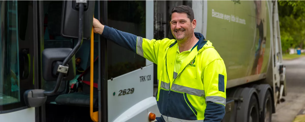 Waste truck driver in hi-vis shirt standing beside truck.