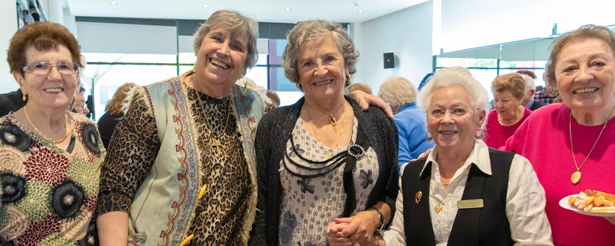 Five women stand smiling together in a community centre.