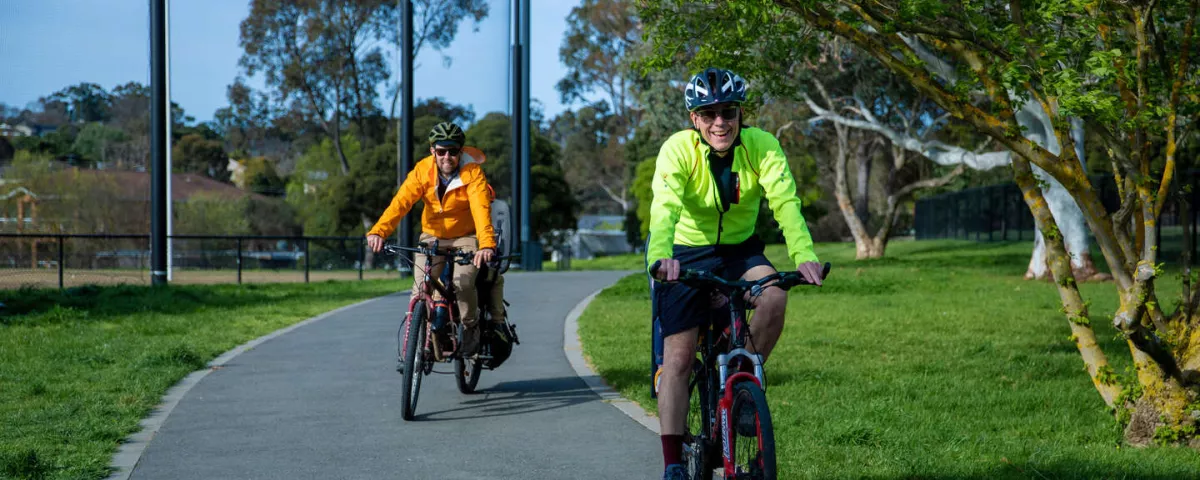 Two people on bikes riding directly towards the camera on a bike path. 